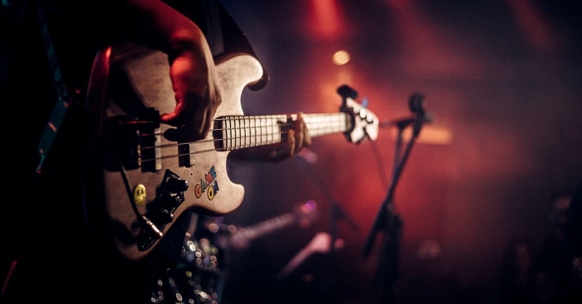 Dynamic image of a guitarist playing at a live music concert, illuminated by colorful stage lights.